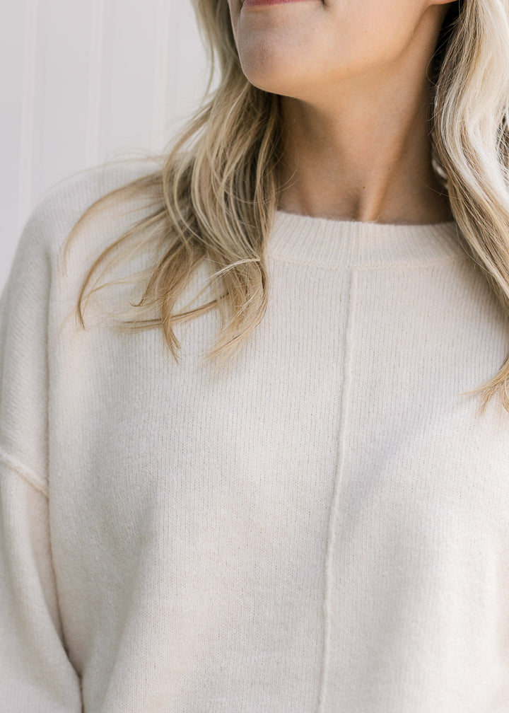 Close up of ribbed detail and exposed hem on a lightweight cream sweater with long sleeves. 