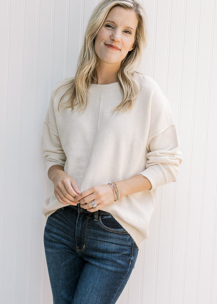 Model wearing a lightweight cream sweater with a round neck and long sleeves pushed up. 