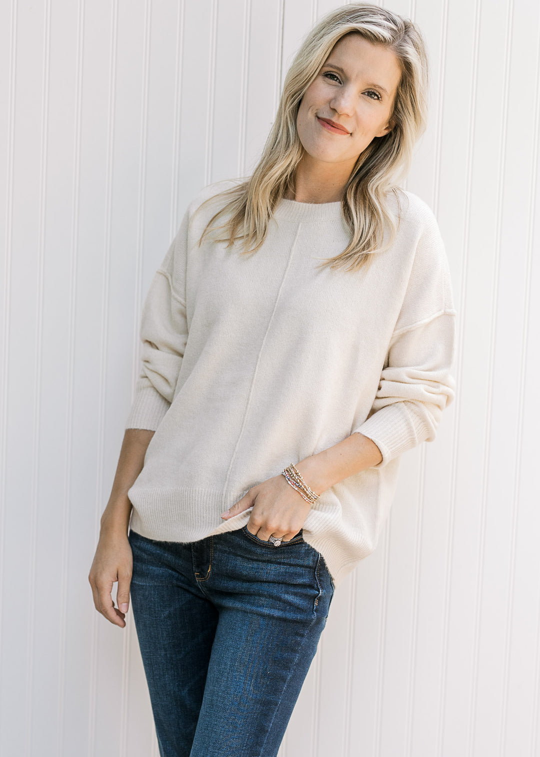 Model wearing a lightweight cream sweater with ribbed detail, exposed hem and long sleeves. 