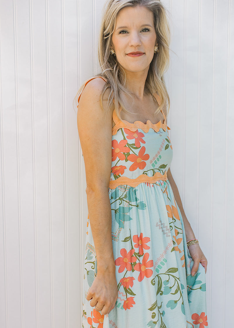 Close up of square neck and soft orange ric-rac trim on a sky blue dress with bright floral. 