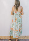 Back view of Model wearing a sky blue dress with bright floral, smocked back and adjustable straps.
