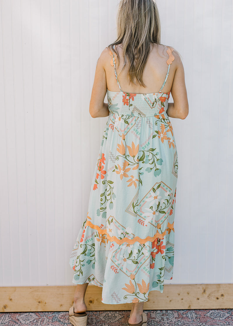 Back view of Model wearing a sky blue dress with bright floral, smocked back and adjustable straps.