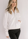 Model wearing an ivory pullover with a 1/4 zip, long sleeves and a front pouch pocket.