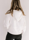 Back view of Model wearing an ivory hoodie with a 1/4 zip, long sleeves and a front pouch pocket.