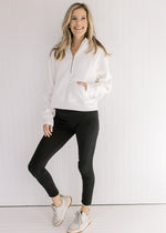 Model wearing workout pants and sneakers with an ivory pullover with a 1/4 zip and long sleeves.
