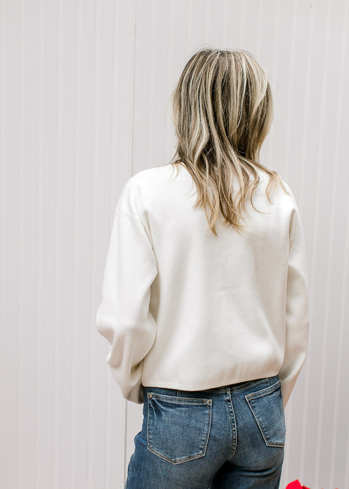 Back view of Model wearing a long sleeve ivory ribbed cardigan with “Merry” written in red script. 