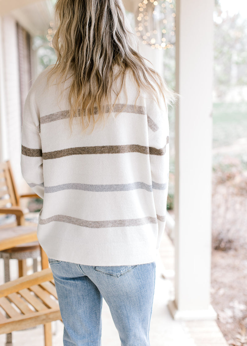 Back view of model wearing an ivory long sleeve sweater with neutral stripes and a crew neck.