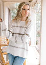 Model wearing jeans and a cream long sleeve sweater with neutral sequin stripes and a crew neck.