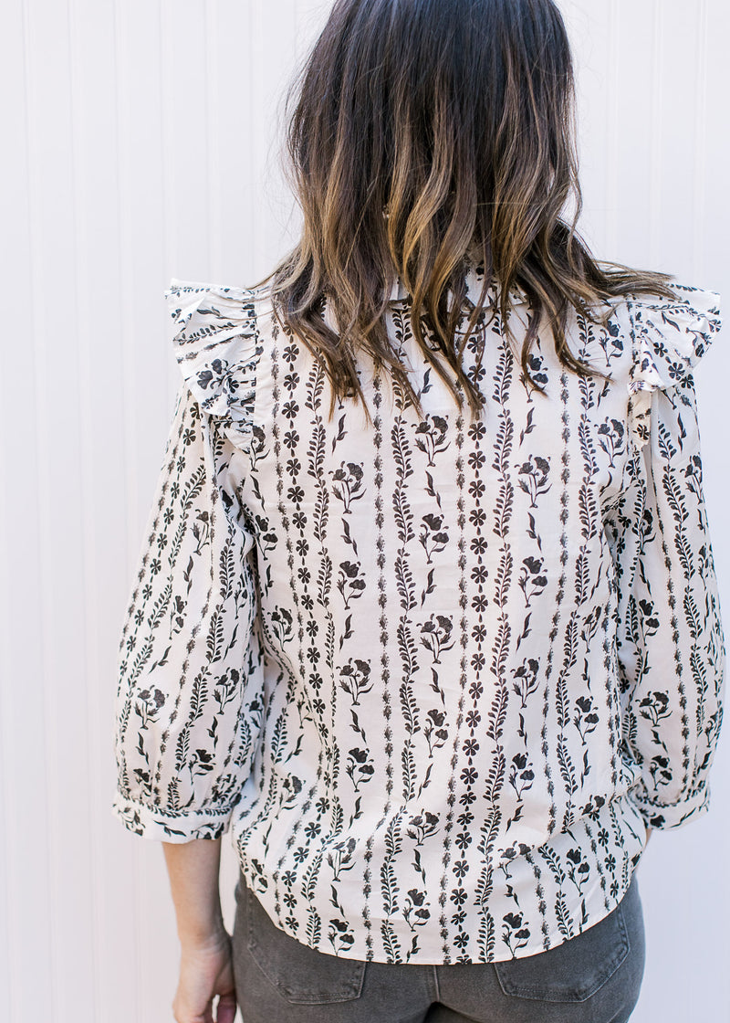 Back view of Model wearing a white top with black floral stripes a v-neck and 3/4 sleeves. 