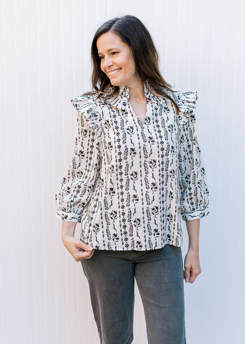 Model wearing black jeans and a white top with black floral stripes, a v-neck and 3/4 sleeves. 