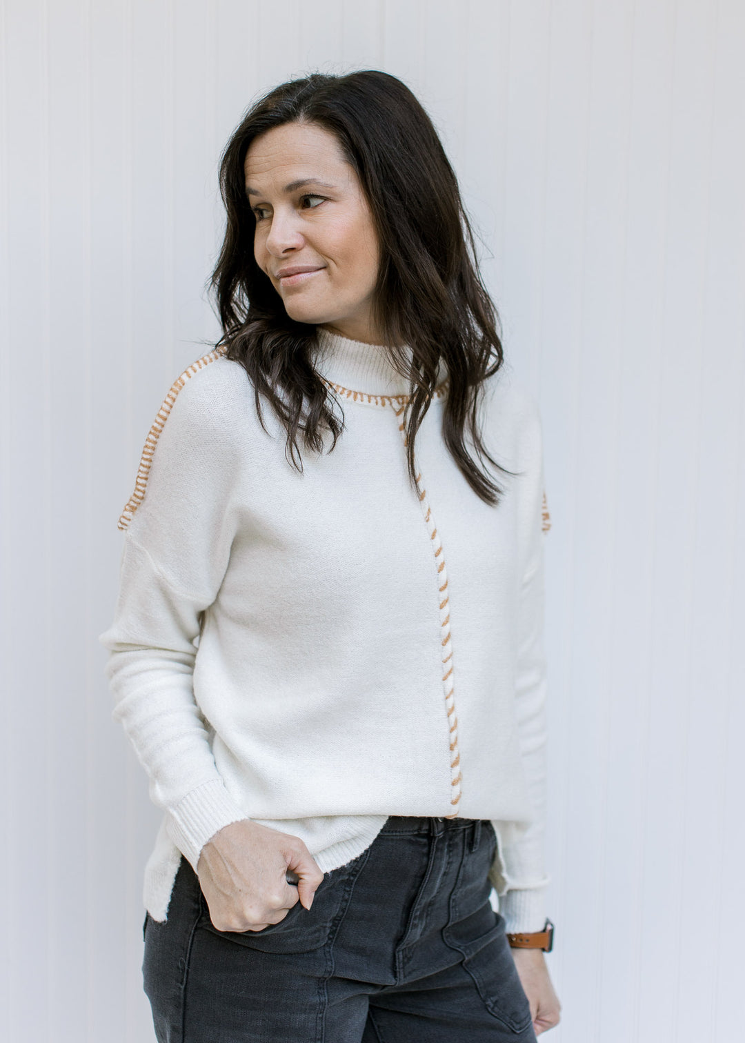 Model wearing a cream sweater with camel contrasting stitch work, long sleeves and a mock neck. 