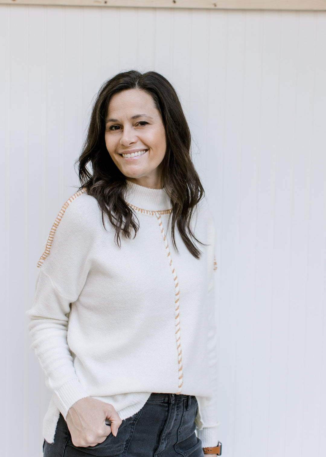 Model wearing a cream sweater with a camel stitch work on exposed hem and long sleeves. 