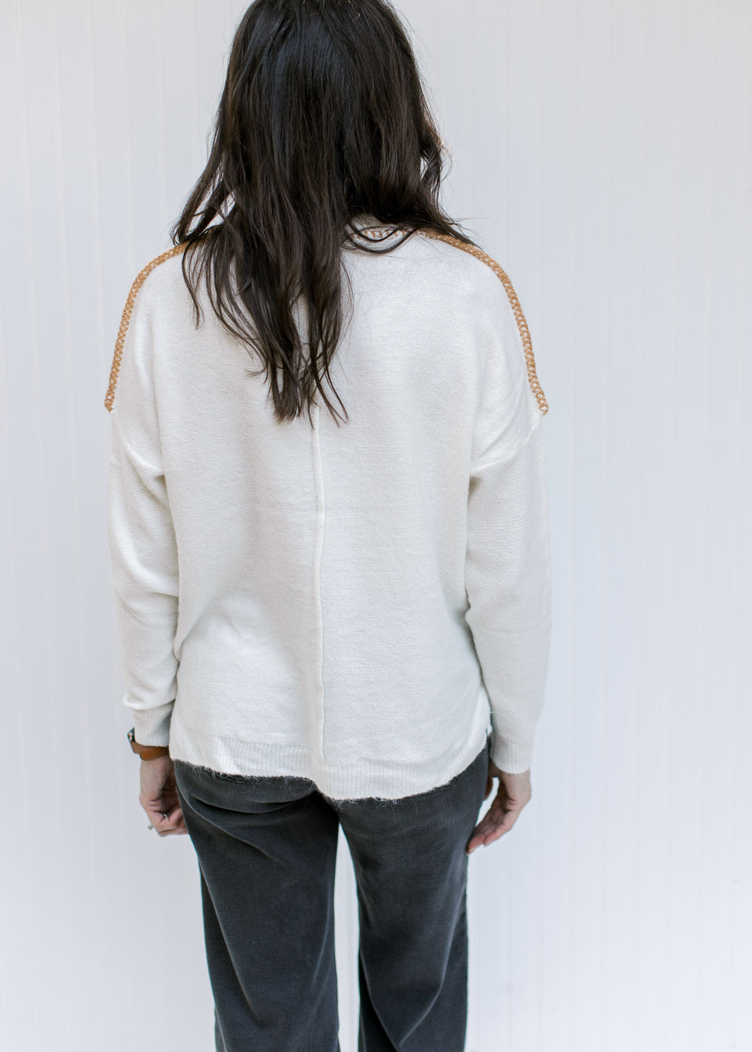 Back view of Model wearing a cream sweater with a camel stitch work on exposed hem and long sleeves.