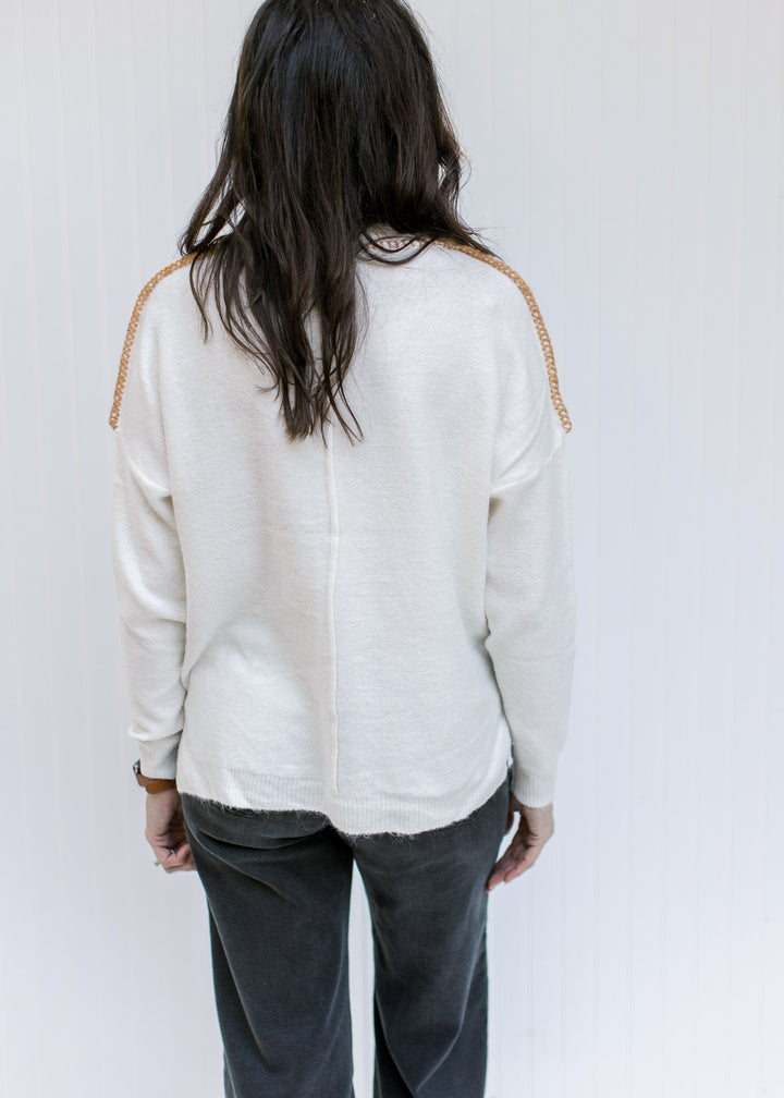 Back view of Model wearing a cream sweater with a camel stitch work on exposed hem and long sleeves.