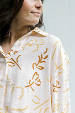 Model wearing a faint pink top with a rust and mustard floral pattern, long sleeves and a button up.