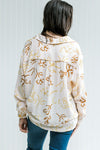 Back view of Model wearing a faint pink top with a rust and mustard floral pattern and long sleeves.