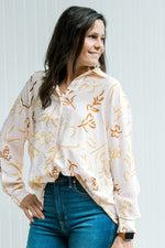 Model wearing jeans with a faint pink button up top with a rust and mustard floral pattern. 