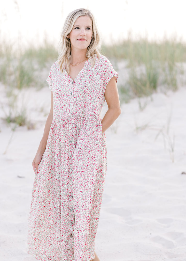 Model wearing an ivory midi dress with a pink floral pattern, button closure and short sleeves.
