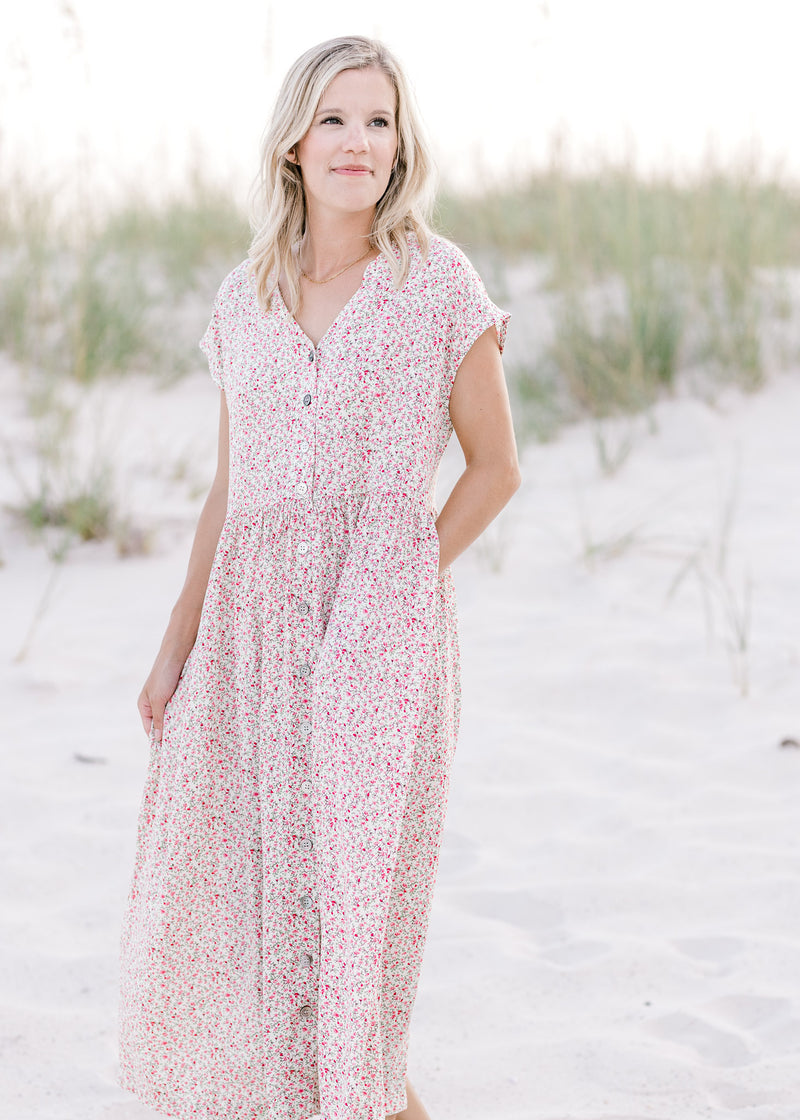 Model wearing an ivory midi dress with a pink floral pattern, button closure and short sleeves.