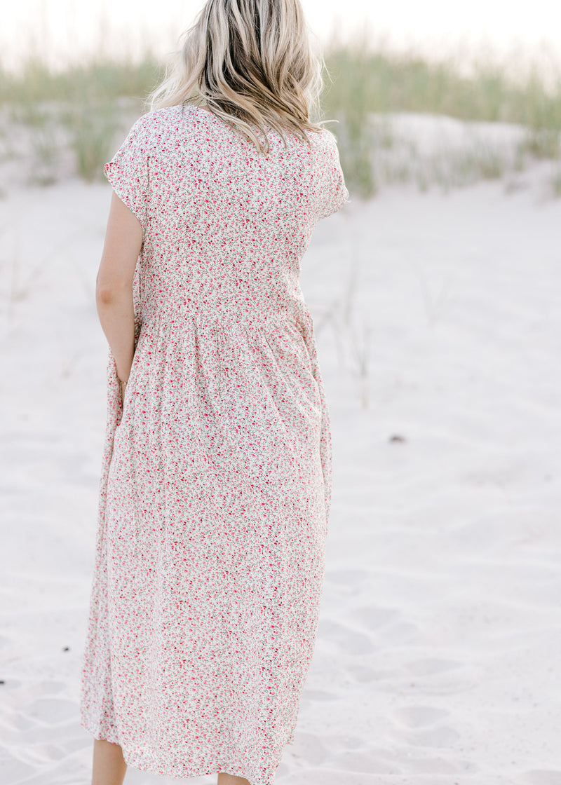 Back view of Model wearing an ivory midi dress with a pink floral pattern and short sleeves.