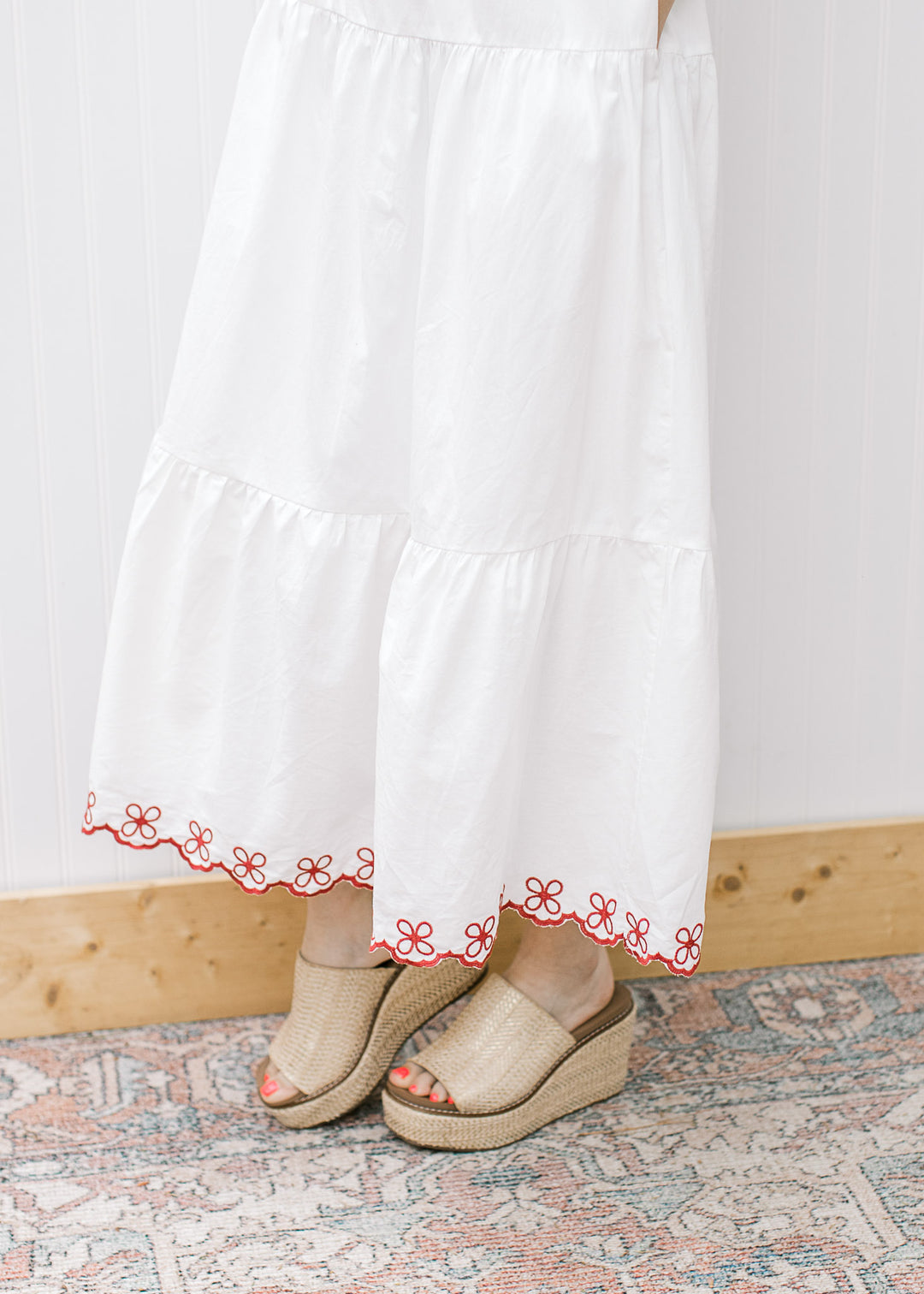 Close up of tiers and maroon floral embroidery on the hem of a white midi and tan wedges. 