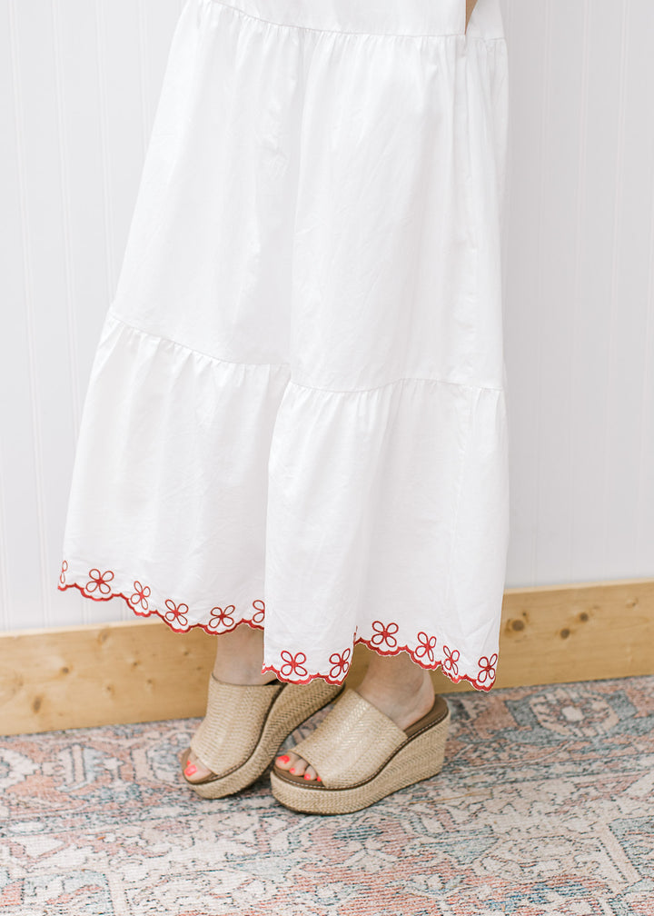 Close up of tiers and maroon floral embroidery on the hem of a white midi and tan wedges. 