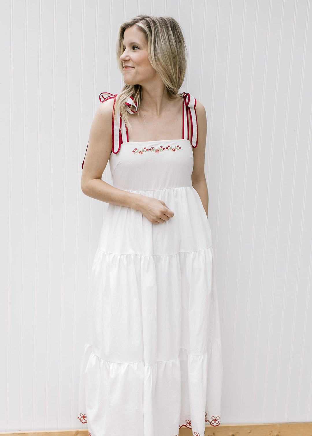 Close up of tie straps and maroon floral embroidery on a white midi with pockets and tiers.