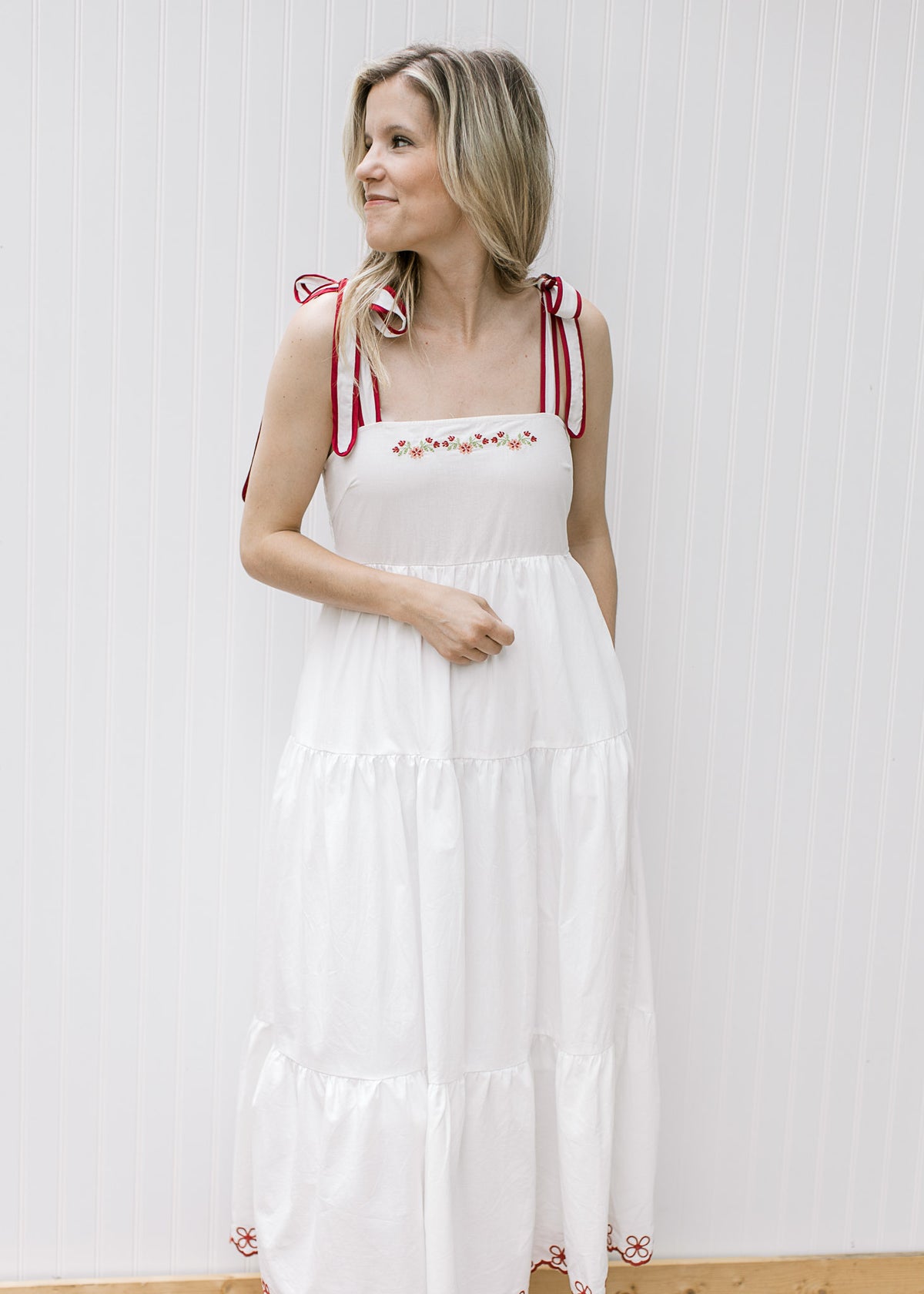 Close up of tie straps and maroon floral embroidery on a white midi with pockets and tiers.