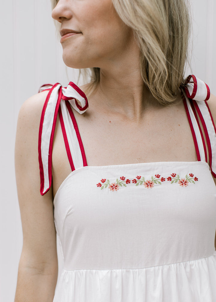 Close up of tie straps and maroon floral embroidery on a white midi with a square neck. 