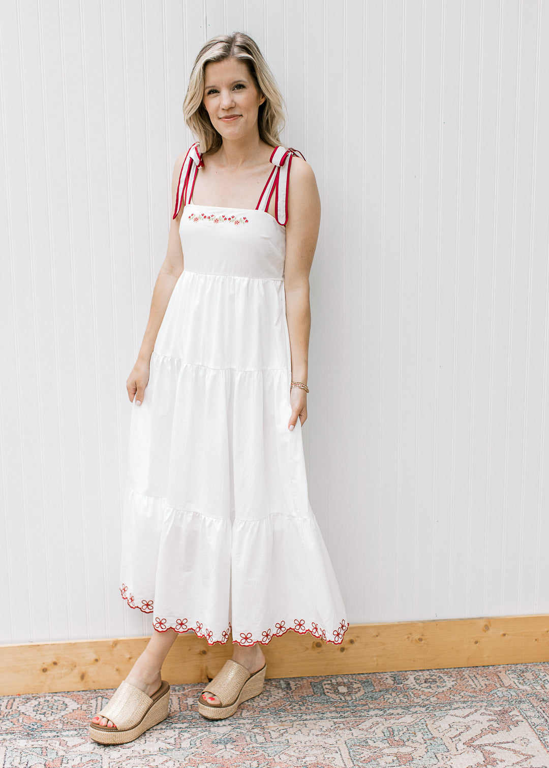 Model wearing a white midi with maroon floral embroidery at neck and hem and a square neck.