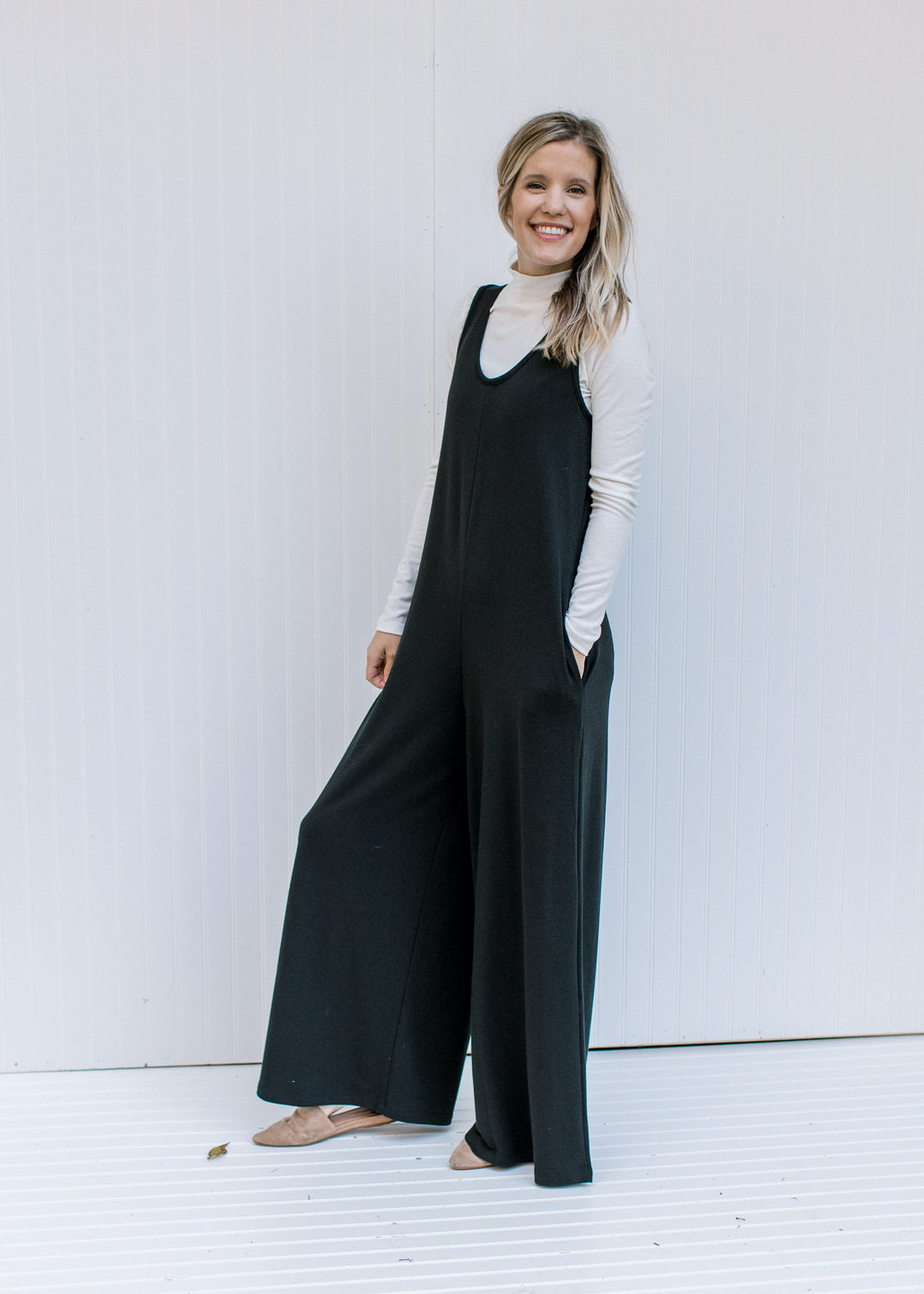Model wearing a jumpsuit with an ivory form fitted top with a mock neckline and long sleeves. 