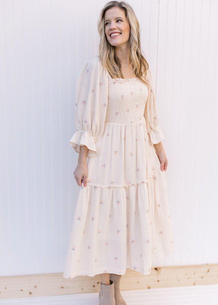 Model wearing an ivory midi with pink flowers, 3/4 poet sleeves and a gauze material. 