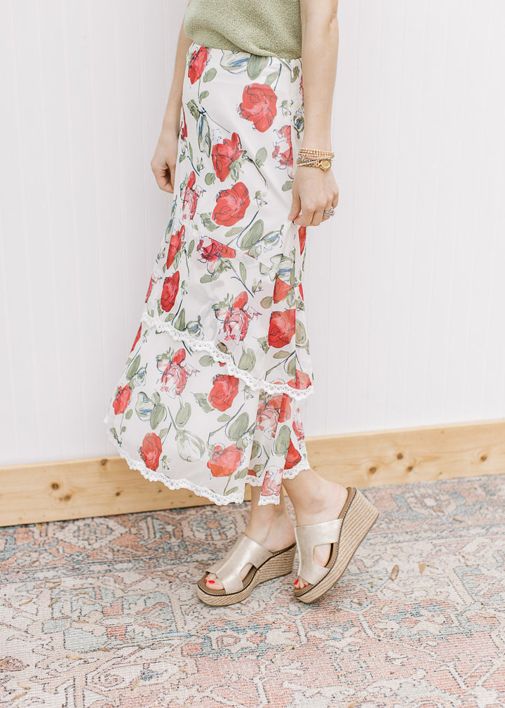 Model wearing an ivory midi with red floral, a tiered silhouette with lace trim and a hidden zipper.