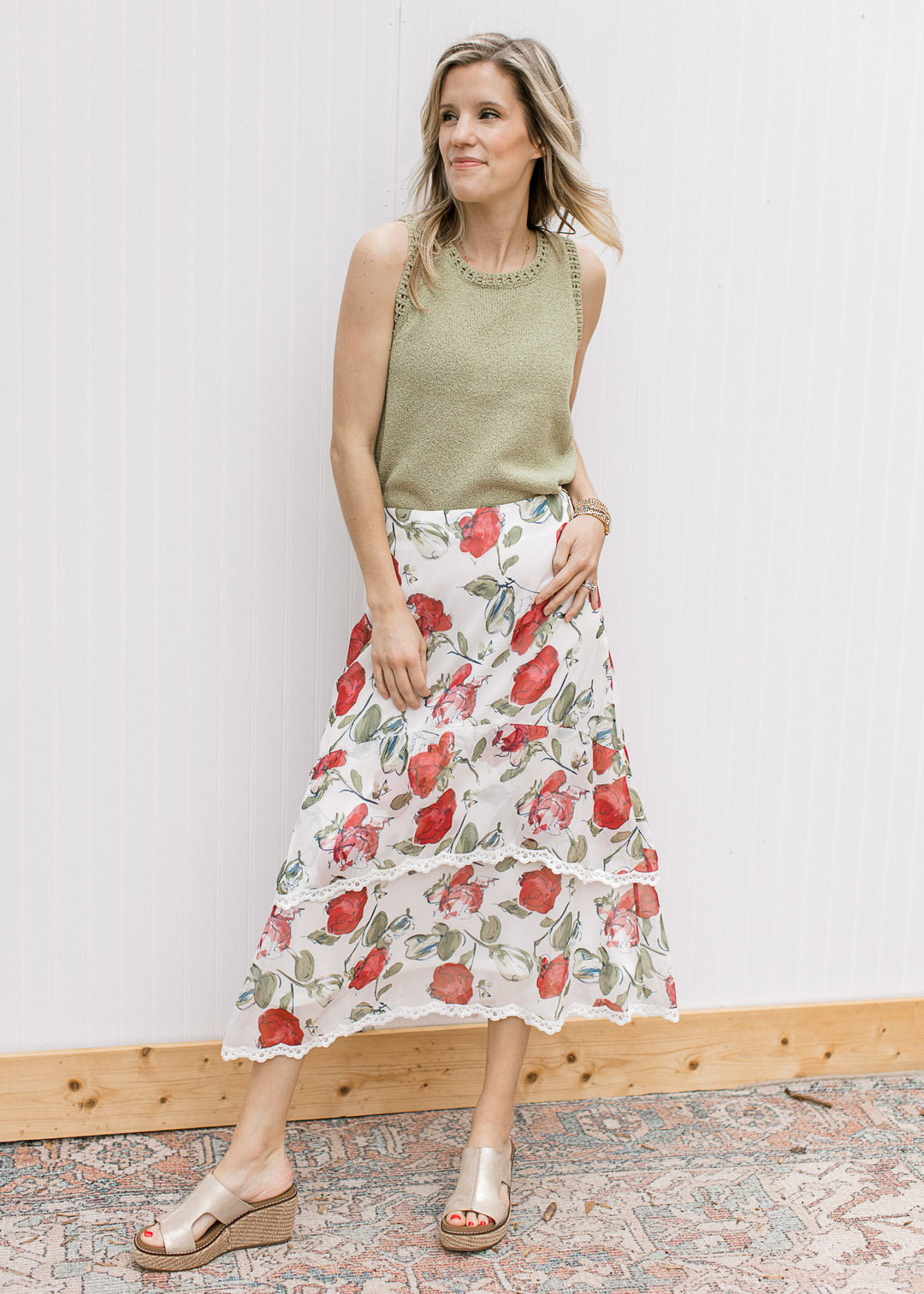 Model wearing a green top, wedges and an ivory midi with red floral print and lace trim tiers.