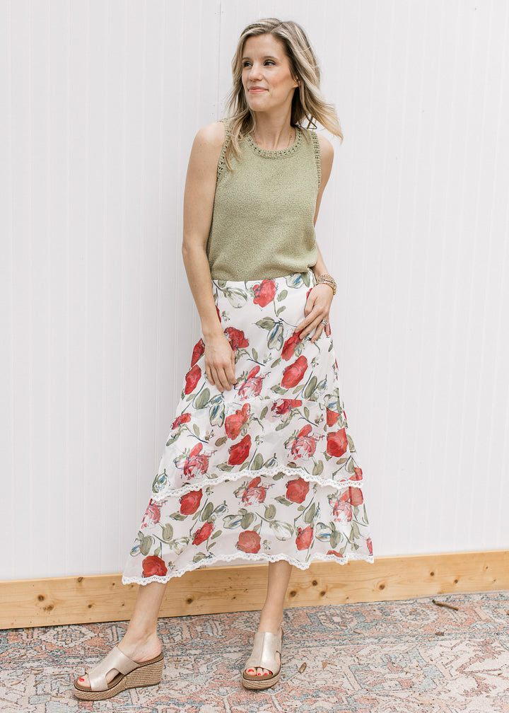 Model wearing a green top, wedges and an ivory midi with red floral print and lace trim tiers.