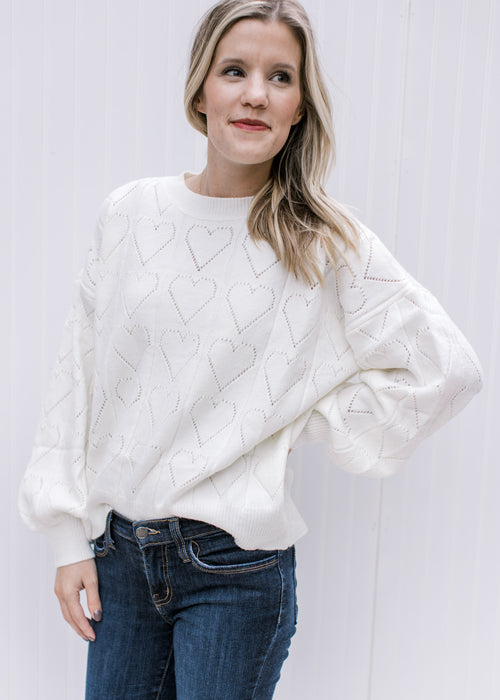 Model wearing an ivory sweater with heart eyelets, long sleeves and a round neck.