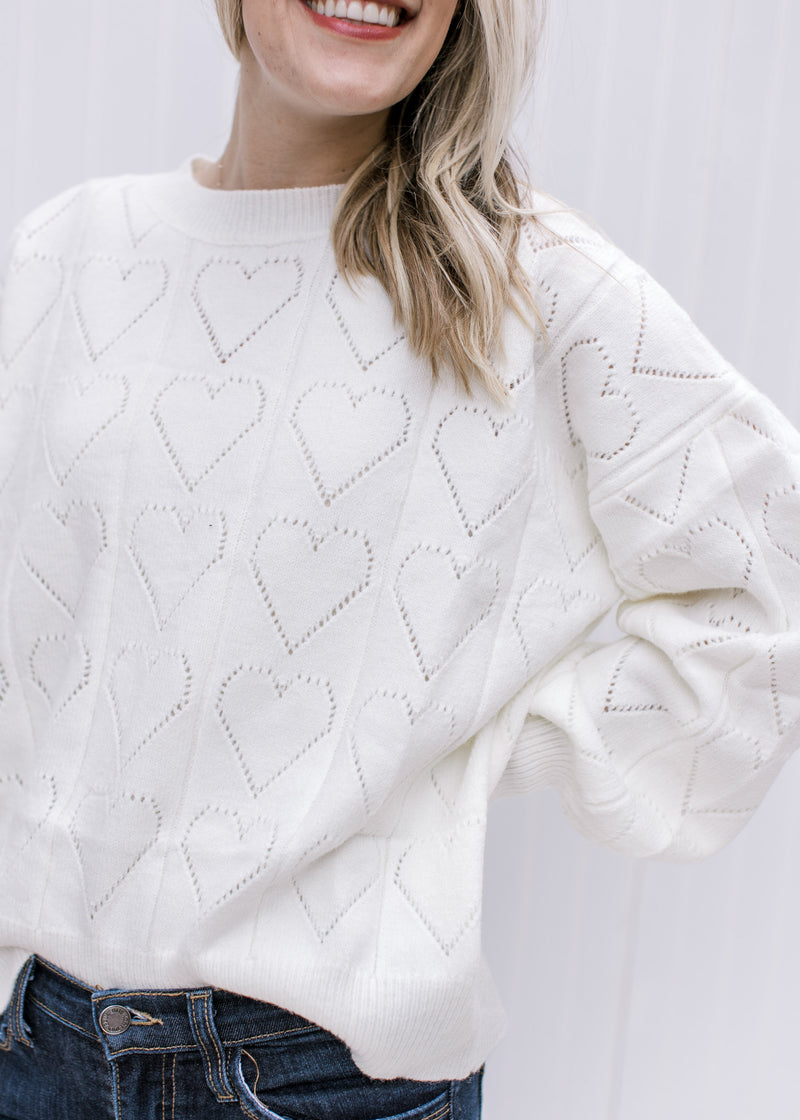 Close up of heart eyelet on an ivory sweater with long sleeves and a round neckline. 