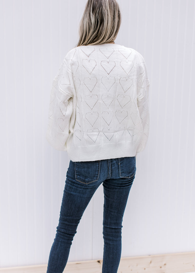 Back view of Model wearing an ivory sweater with heart eyelets, long sleeves and a round neck.