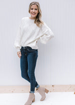 Model wearing jeans, booties and an ivory sweater with heart eyelets, long sleeves and a round neck.