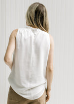 Back view of a model wearing an ivory top with a ruffle at the neck and a keyhole closure.