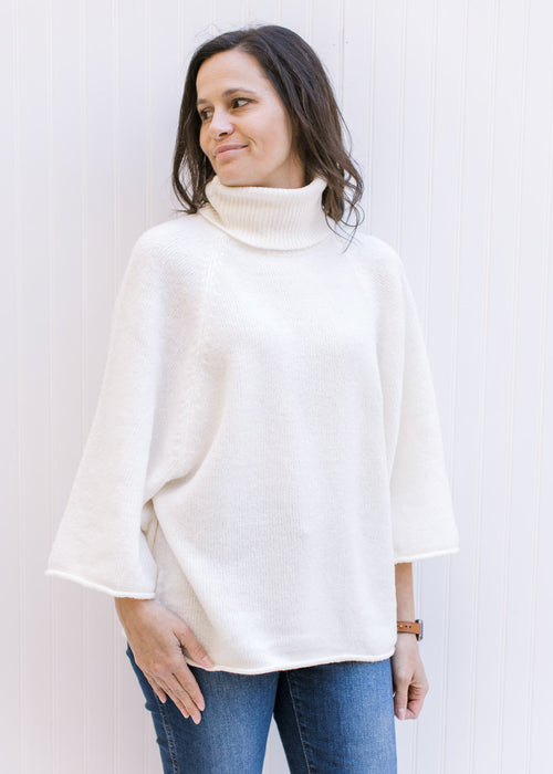 Model wearing an ivory soft yarn sweater with a loose turtle neck and 3/4 sleeves. 