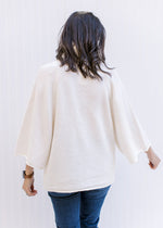 Back view of Model wearing an ivory soft yarn sweater with a loose turtle neck and 3/4 sleeves.