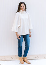 Model wearing jeans and mules with an ivory soft yarn sweater with loose turtleneck and 3/4 sleeves.