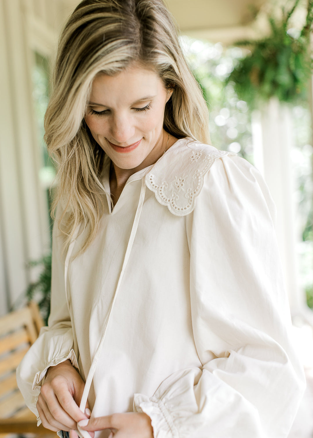 Model wearing an ivory top with a v-neck, a wide eyelet collar and long sleeves with elastic.