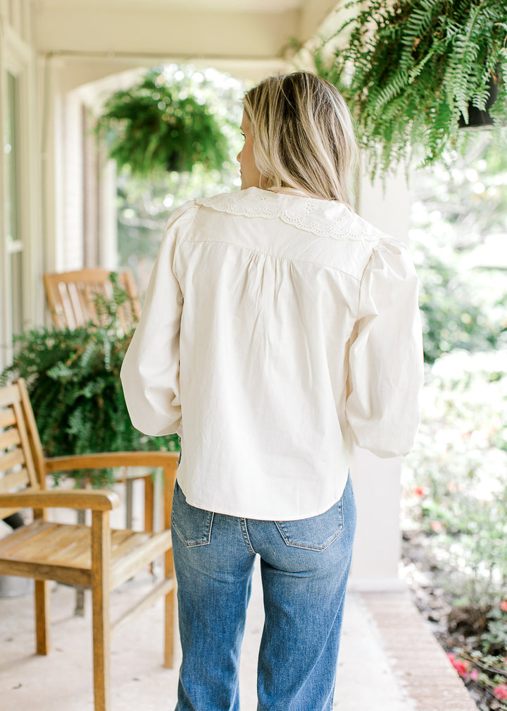 Back view of Model wearing an ivory top with a wide eyelet collar and long sleeves with elastic.