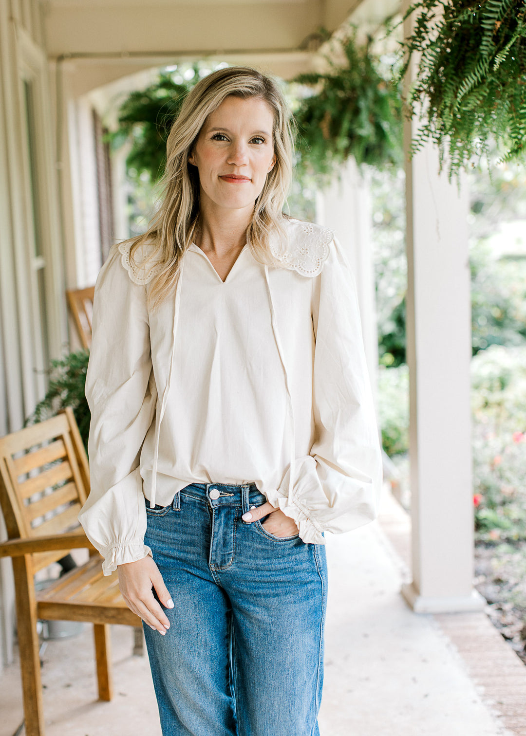 Model wearing jeans and an ivory top with a v-neck, a wide eyelet collar and long sleeves.