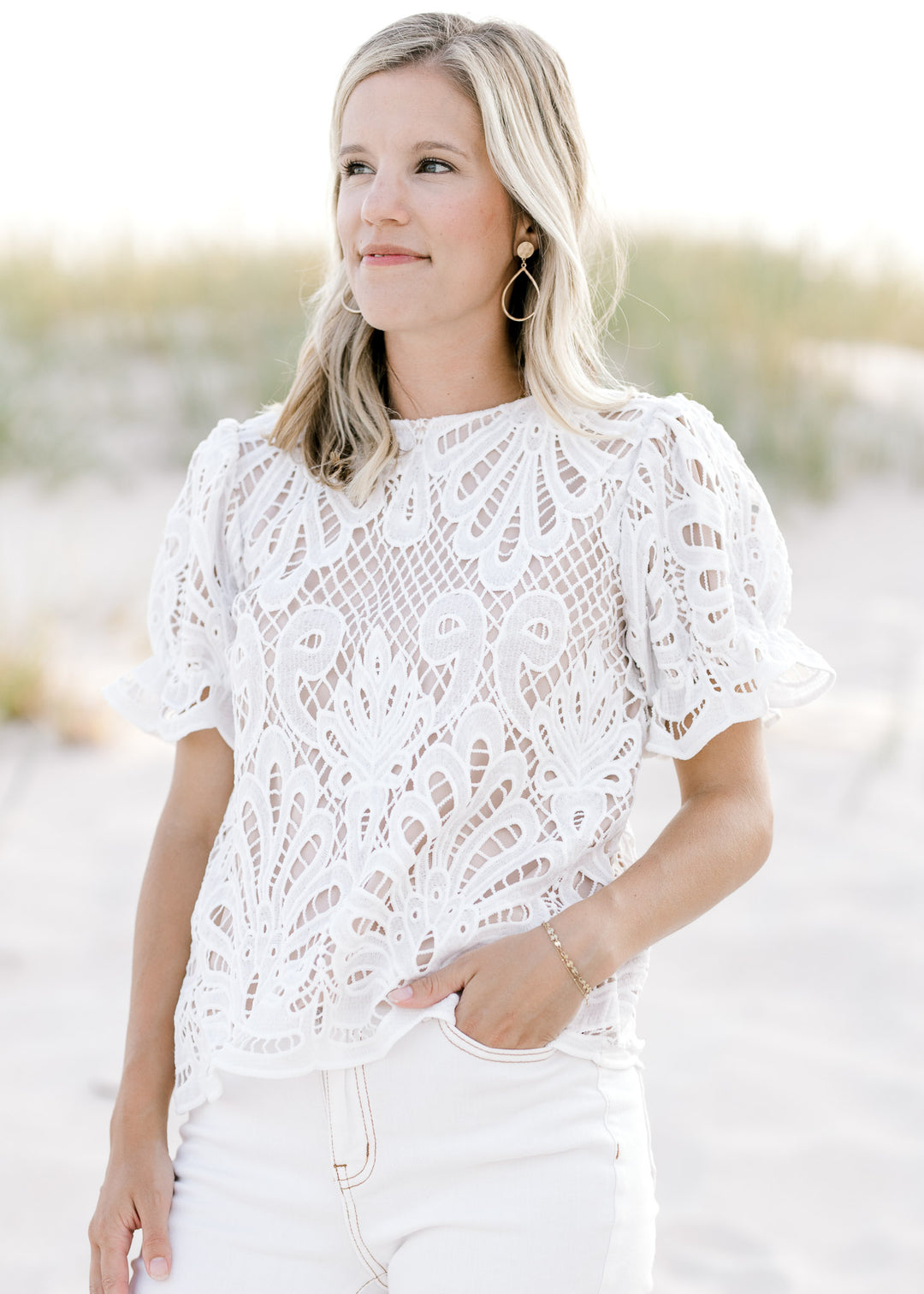Model wearing a nude short sleeve top with an ivory lace overlay, a round neck and keyhole closure. 