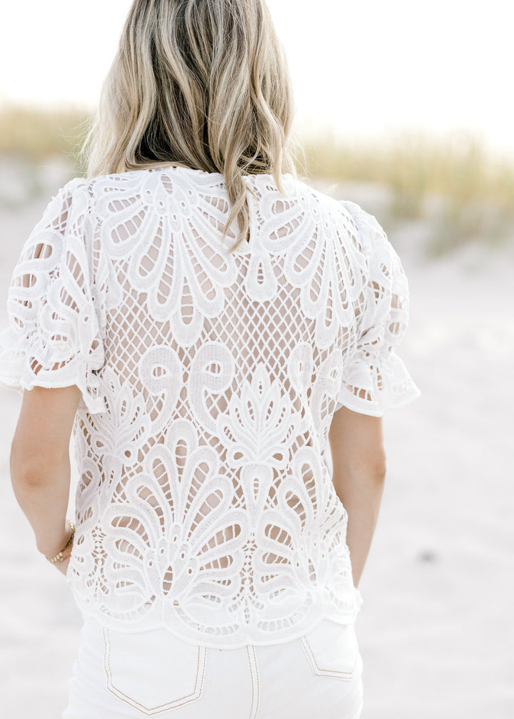 Back view of Model wearing a nude top with an ivory lace overlay and a keyhole closure. 
