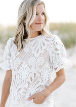 Model wearing a nude short puff sleeve top with an ivory lace overlay and a round neck. 