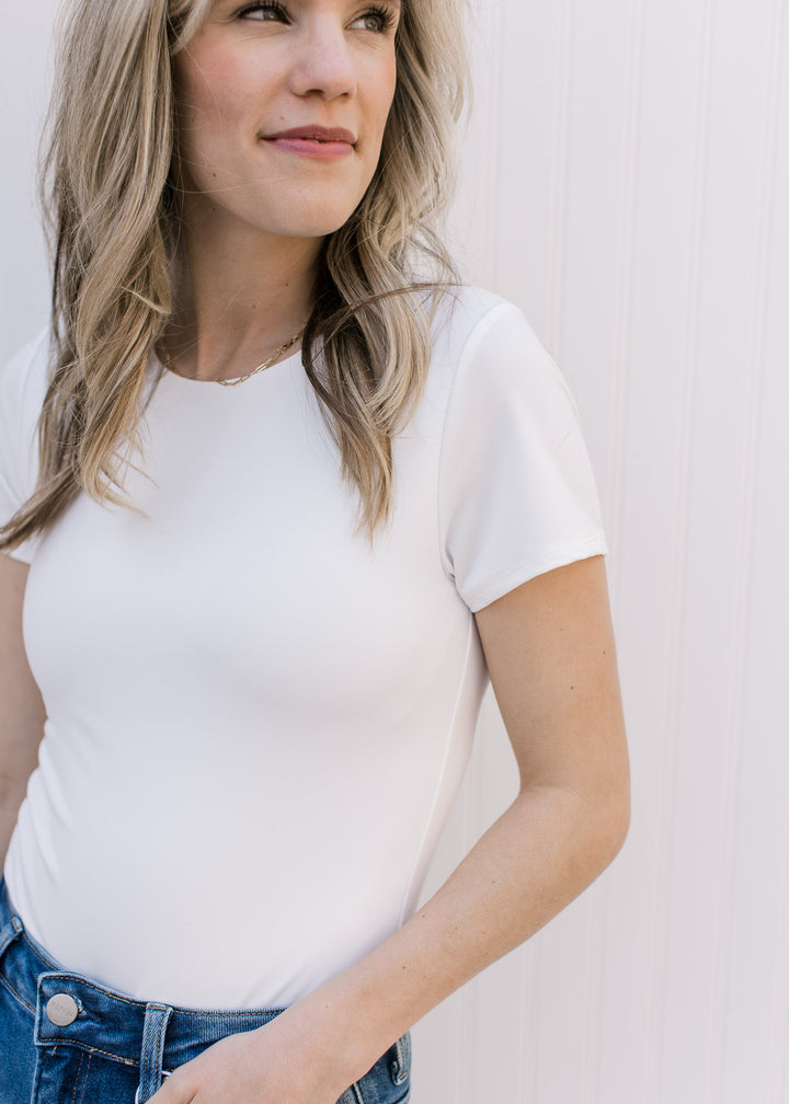 Model wearing a short sleeve ivory bodysuit with a double clasp closure and a crew neck.
